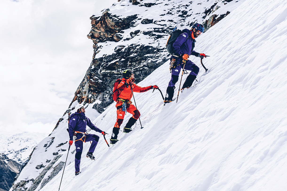 Alpine climbers wearing technical apparel while trekking up a snow summit